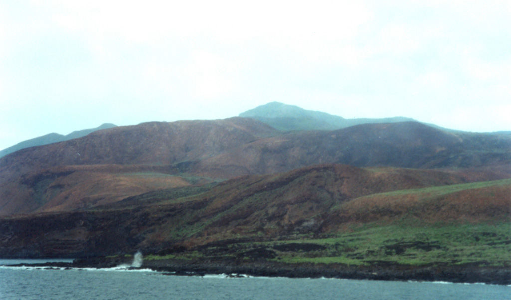 The northern, western, and southern flanks of Socorro are dominated by silicic lava domes and flows, which cover about 80% of the surface of the island. This view shows Cerro Evermann from the SW coast. Trachyte and rhyolite lava flows from summit and flank vents extend into the sea and have produced an irregular shoreline, with the distal portions of lava flows forming numerous small peninsulas. Photo by Martha Marin, 1998 (Mexican Navy).