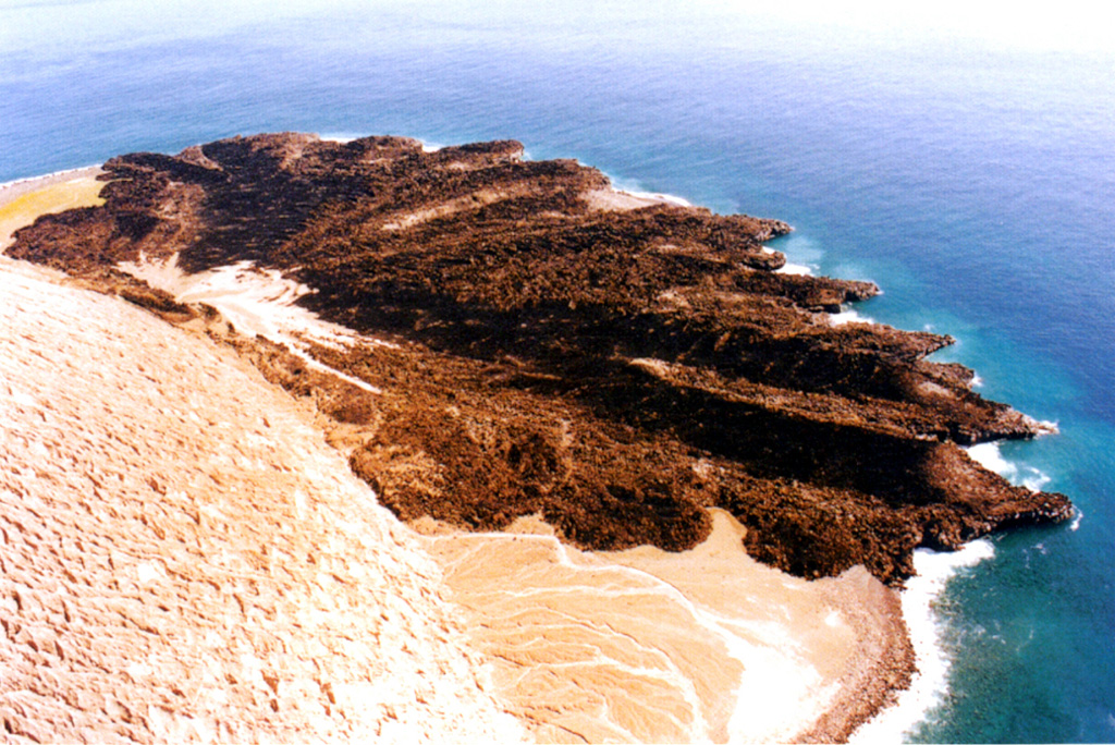 Wave erosion rapidly modified the once smooth coastal margin of the lava delta that erupted in 1952-53. The vent that produced the flow is to the left at the base of the light-colored tuff cone that also formed during the eruption. The Delta Lávico flow extended 700 m out to sea and formed a peninsula about 1.2 km wide. Photo by Hugo Delgado-Granados, 1993 (Universidad Nacional Autónoma de México).