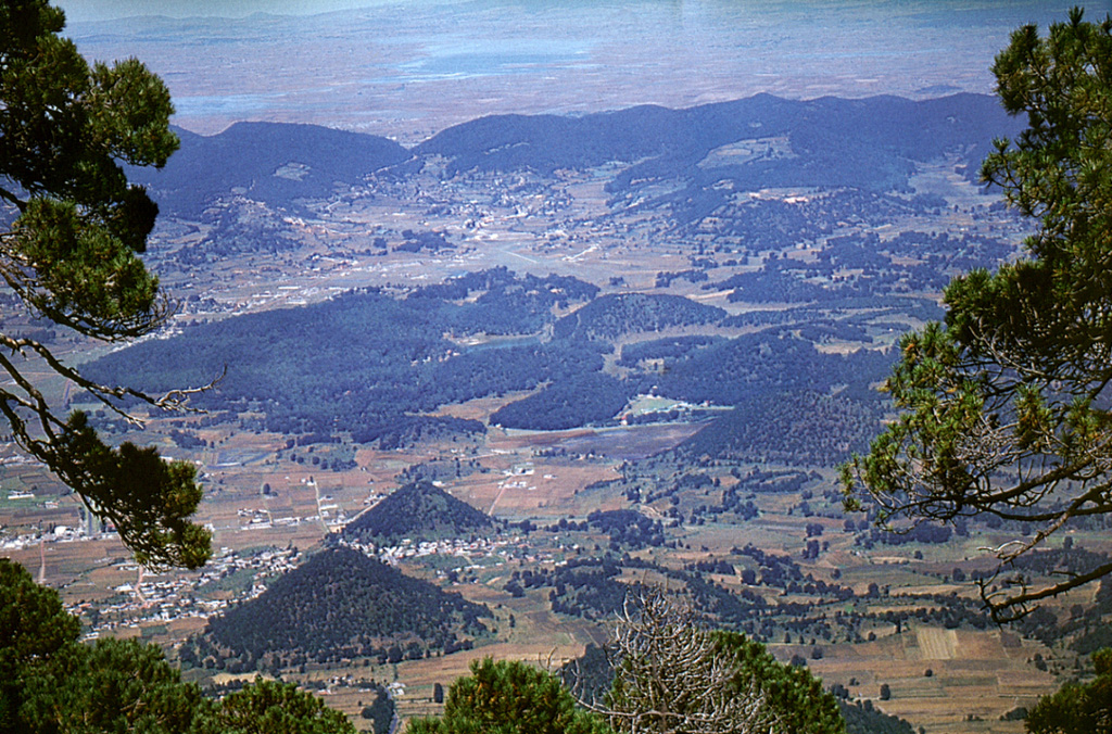 The tree-covered hills in the foreground and center of this view from the summit of Jocotitlán volcano were formed during a massive debris avalanche produced by collapse of the volcano about 9,700 years ago. The debris avalanche deposit includes several conical hummocks (such as those to the lower left) and large transverse ridges up to 2.7 km long. The avalanche traveled a maximum distance of 12 km to the NE and covered an area of 80 km2. Photo by Hugo Delgado-Granados, (Universidad Nacional Autónoma de México).