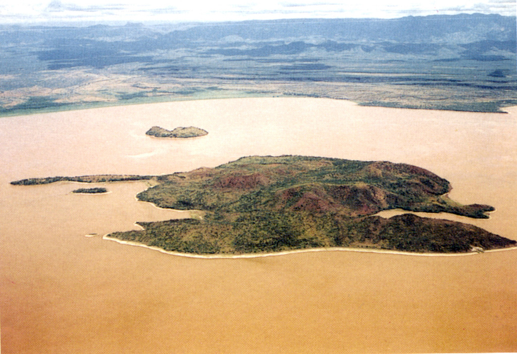 Ol Kokwe Island in Lake Baringo is seen in an aerial view looking W towards the Saimo escarpment of the rift margin. The elongated Island consists of young basaltic scoria cones that cap a trachytic shield volcano. N-S-trending faults cut the island, forming the double-tipped peninsula in the foreground and the narrow peninsula at the left center. The smaller island beyond Ol Kokwe is Parmalok, a tuff cone that fed a small lava flow. Photo by Martin Smith, 1993 (copyright British Geological Survey, NERC).