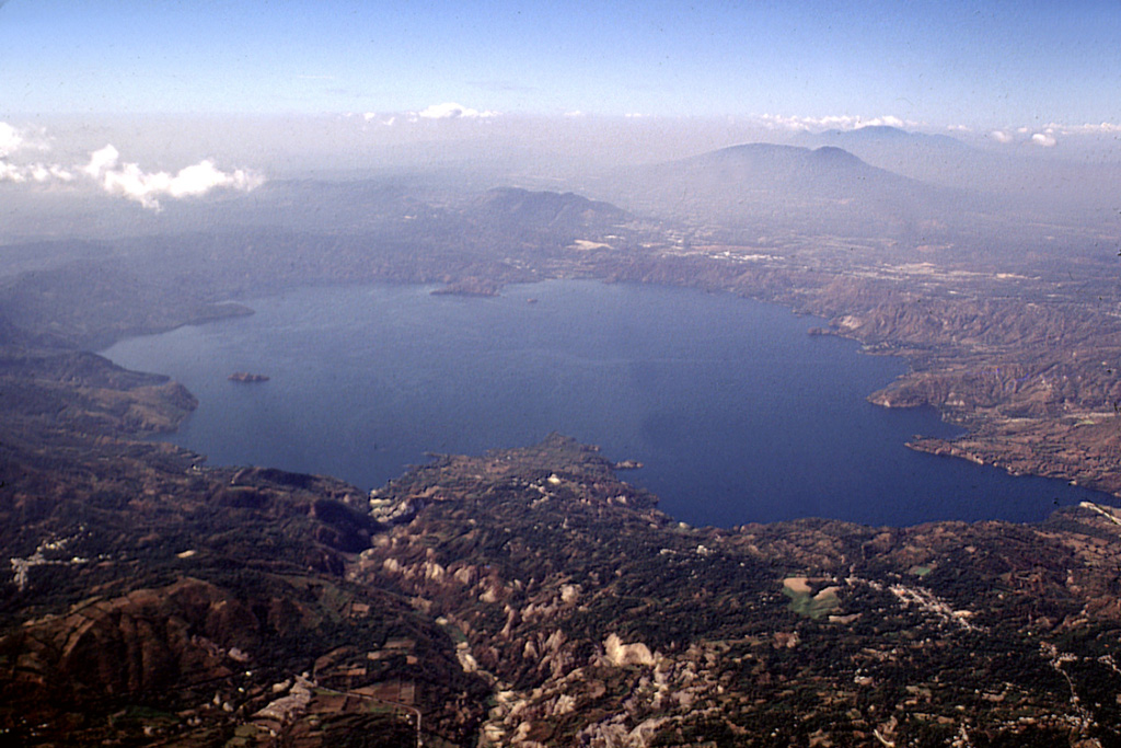 The 8 x 11 km wide Ilopango caldera fills the center of the image in this view from the ESE. Fresh, light-colored exposures of the Tierra Blanca Joven formation in the foreground associated with the latest caldera-forming episode were in part created by landslides during the January 2001 earthquake. The capital city of San Salvador lies beyond the lake, in front of San Salvador volcano (upper right). The Santa Ana volcanic complex lies beyond San Salvador volcano in the background to the far right. Photo by Lee Siebert, 2002 (Smithsonian Institution).