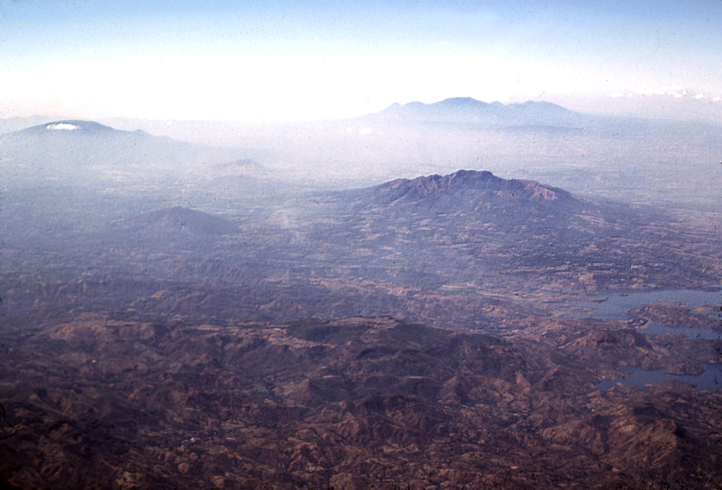 Volcán de Guazapa (near the center) rises beyond the Cerrón Grande reservoir (lower right) in this view from the NE. The smaller cone to the left of Guazapa is Cerro Tecomatepe. San Salvador volcano is to the upper left, the Santa Ana complex is the broad massif at the upper right, and peaks of the Sierra Apaneca near the Guatemalan border form the irregular ridge to the far right. Photo by Lee Siebert, 2002 (Smithsonian Institution).