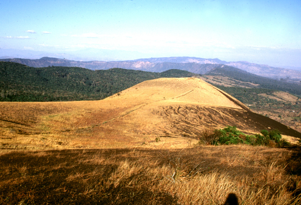 San Marcelino scoria cone is seen from Cerro Chino on the SE flank of Santa Ana. San Marcelino formed during an eruption in 1722 and produced a lava flow that traveled 13 km to the east. The vegetated southern rim of Coatepeque caldera can be seen to the NE (left) of San Marcelino. Photo by Lee Siebert, 2002 (Smithsonian Institution).