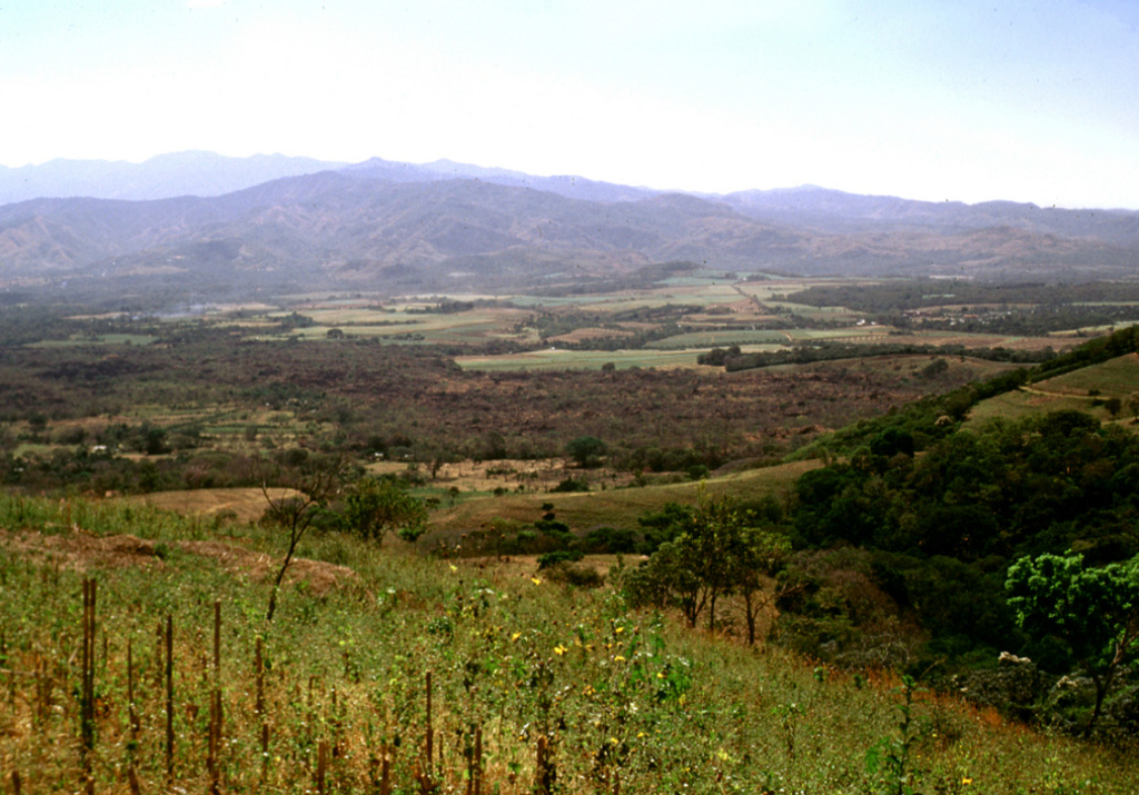 The brownish area extending across the center of the photo is the 1722 Teixcal lava flow. Erupting from the base of San Marcelino scoria cone on the SE flank of Santa Ana (out of view to the right), the flow traveled 13 km E to the edge of the Zapotitán basin and destroyed the village of San Juan Tecpán as well as burying about 15 km2 of agricultural land.  Photo by Lee Siebert, 2002 (Smithsonian Institution).
