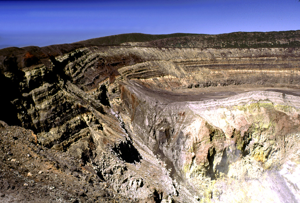 Sequences of phreatomagmatic tephra layers are exposed in the southern and western crater walls of Santa Ana. The hydrothermally altered area to the lower right is the inner crater, which contains an acidic lake not visible in this photo. Four crater walls can be seen in this photo; the two outer walls appear in the center on and below the horizon, beyond the flat rim of the inner crater. Photo by Lee Siebert, 2002 (Smithsonian Institution).