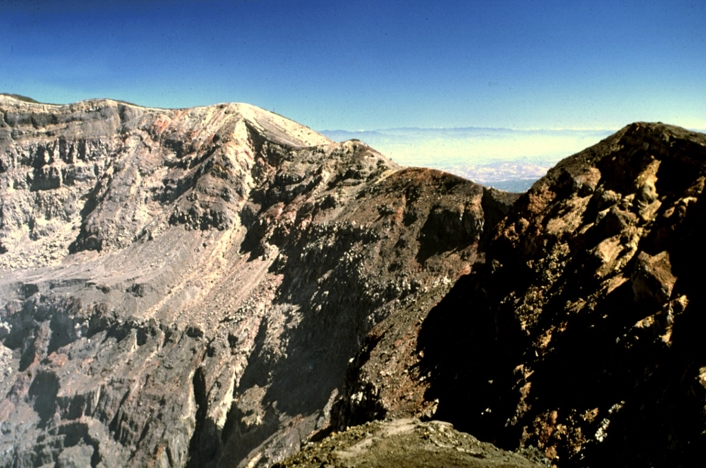 The eastern crater rim of Santa Ana rises more than 100 m above the crater floor. The eastern wall is composed of breccias, scoria units, thin lava flows, and dikes. Thick sequences of lava flows are exposed in the northern and southern crater walls and on the southern side they are overlain by phreatomagmatic tephra layers up to 100 m thick. Photo by Lee Siebert, 2002 (Smithsonian Institution).