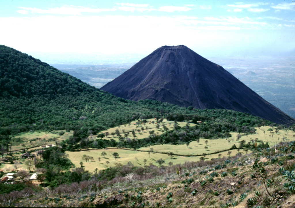 Izalco volcano rises beyond the Cerro Verde flank to the left, as seen from the trail to the summit of Santa Ana. Hotel de la Montaña was constructed at the summit of Cerro Verde to provide a view of the Izalco erupting, which occurred frequently since 1770. By the time the hotel was completed, the eruption of Izalco had ended. Photo by Lee Siebert, 2002 (Smithsonian Institution).