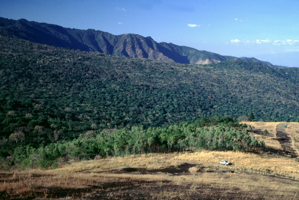 This view shows the western side of Coatepeque caldera (top of the photo) from Cerro Chino scoria cone on the SE flank of Santa Ana, which lies out of view to the left. The caldera rim partially cuts into the eastern side of Santa Ana. The western side of Coatepeque caldera is considered to have formed during the second stage of caldera formation through a lake partially filling the earlier caldera, producing the Congo Formation tephras and pyroclastic flows. Photo by Lee Siebert, 2002 (Smithsonian Institution).