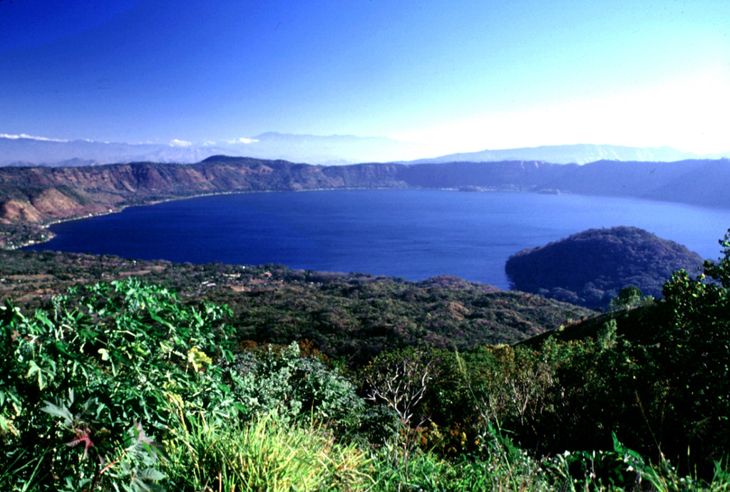 This view from the road to the Cerro Verde summit shows the eastern side of Coatepeque caldera. The hill in the lake (right) is the Cerro Grande lava dome. The caldera formed during two major explosive eruptions, the first of which occurred about 72,000 years ago, forming the eastern part of the caldera in association with the Arce pumice fall and pyroclastic flow deposits. A lake partially filled the caldera floor prior to the Congo eruption associated with formation of the western part of the caldera. Photo by Lee Siebert, 2002 (Smithsonian Institution).