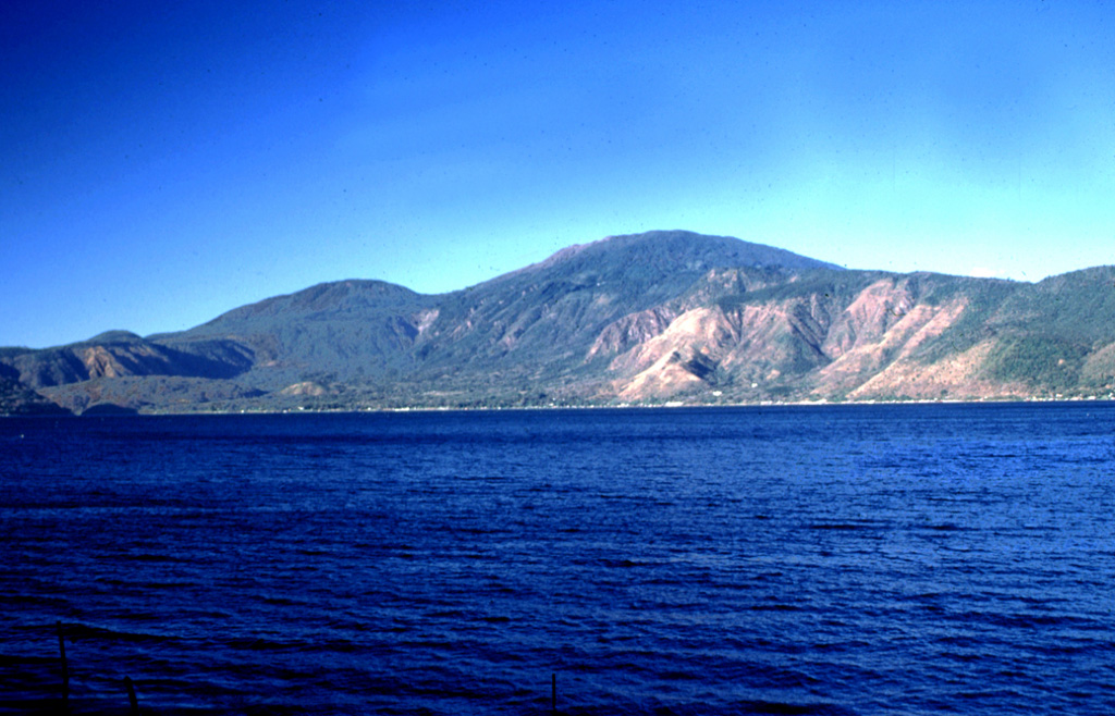 Santa Ana volcano rises above Lago de Coatepeque. The 6-km-wide lake lies at the eastern end of the Coatepeque caldera. The northern and southern rims of the western side of the caldera are visible beyond the lake. The rounded peak to the left of Santa Ana is Cerro Verde, one of many cones along a NW-SE-trending fissure cutting across the Santa Ana complex. Photo by Lee Siebert, 2002 (Smithsonian Institution).