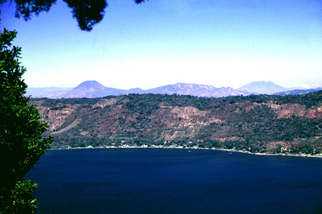 The northern wall of Coatepeque caldera rises about 250 m above the surface of Lago de Coatepeque, whose shores are lined with residences and small hotels. The peak beyond the caldera to the left is Volcán Chingo along the El Salvador/Guatemala border. The broader peak to the far right is Volcán Suchitán, one of the largest volcanoes in SE Guatemala.  Photo by Lee Siebert, 2002 (Smithsonian Institution).