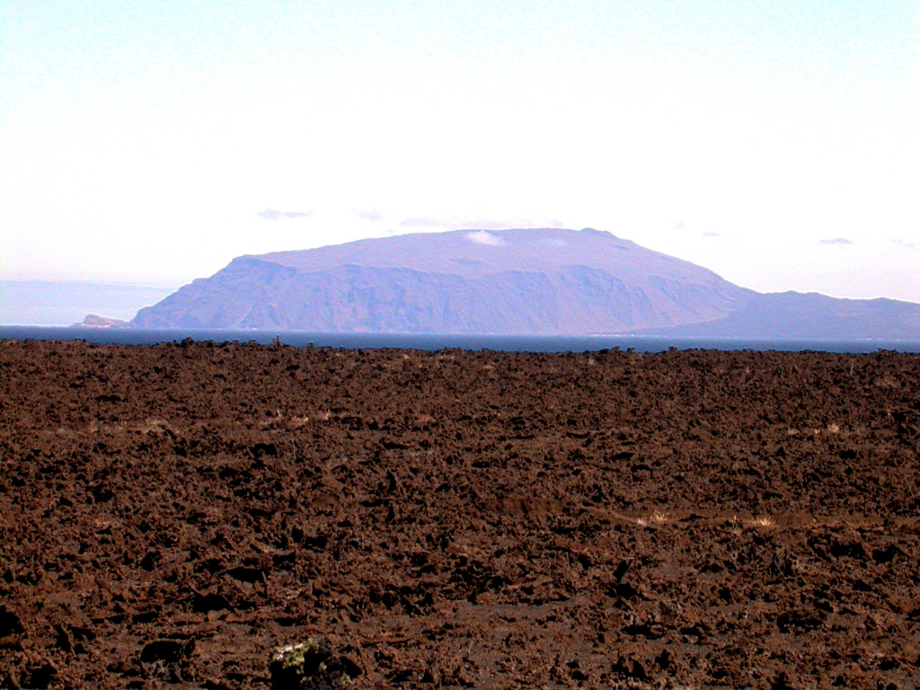 Volcán Ecuador, which straddles the equator at the NW end of Isabela Island, rises beyond a lava flow near Beagle tuff cone on the flanks of Darwin volcano.  Ecuador is the smallest of the six large shield volcanoes on Isabela and is broadly breached to the coast on the side opposite this view.  No historical eruptions are known; however, the youthful morphology of its most recent lava flows resembles those of very recent flows on other Isabela Island volcanoes.  A line of NE-trending fissure-fed vents (right horizon) extends to the SE. Photo by Ed Vicenzi, 2002 (Smithsonian Institution).