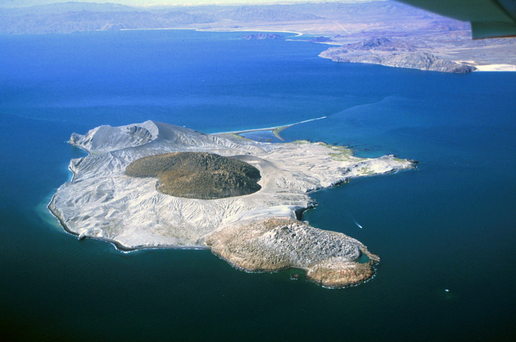 Isla San Luis lies across a narrow channel from the NE coast of Baja California (in the background). A rhyolite obsidian dome is in the center of the small island. An older dome forms the northern part of the island (foreground) and is partially mantled by ash and pumice from the central dome. An eroded tuff ring, Plaza de Toros, occupies the SE end of the island. Photo by Keith Sutter, 2000.