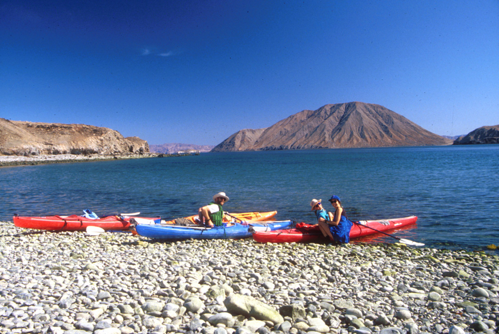Volcán Coronado (back right) rises behind a group of kayakers across the Canal de los Ballenas in this 1994 photo. The small cone is about 2 km wide with a 300 x 160 m crater at the northern end of Coronado Island, 3 km off the eastern coast of Baja California. Photo by Brian Hausback, 1994 (California State University, Sacramento).