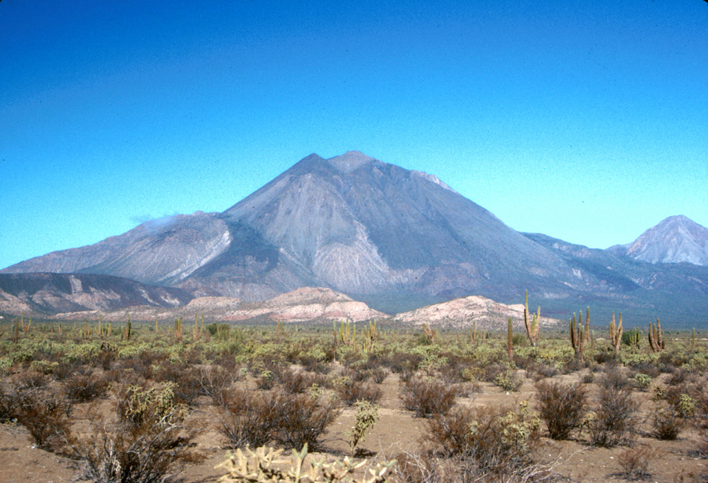 The Tres Vírgenes volcanic complex in central Baja California consists of a NE-SW-trending chain of three volcanoes, seen here from the SE. Volcanism has migrated over time to the SW. El Azufre is the intermediate-age cone to the right and La Vírgen is to the left. The latest major eruption produced a Plinian pumice fall deposit and thick lava flows from a vent near the ridge seen halfway up the SW flank (left). Photo by Brian Hausback, 1990 (California State University, Sacramento).