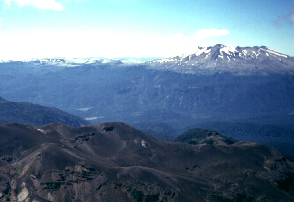 The Puyehue-Cordón Caulle volcanic complex forms the horizon in this view looking north across the Río Gol Gol valley from the Antillanca volcano group.  Flat-topped 2236-m-high Puyehue volcano (right) is a late-Pleistocene to Holocene basaltic-to-rhyolitic stratovolcano constructed above a 5-km-wide caldera and capped by a 2.4-km-wide summit caldera.  Historical eruptions originally attributed to Puyehue are now known to be from the Cordón Caulle rift zone, the long snow-covered ridge that extends across the photo to the left of Puyehue. Photo by Klaus Dorsch, 2001 (University of Munich).