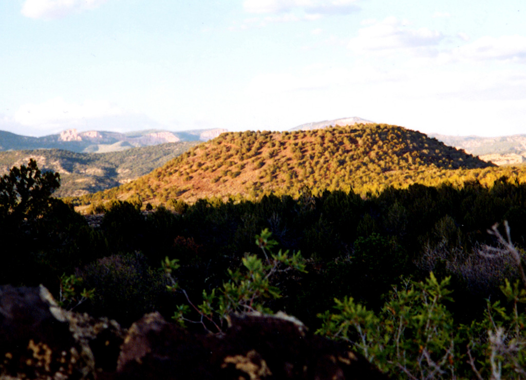 Bald Knoll is the youngest of a group of cinder cones on the SW part of the Paunsaugunt Plateau in southern Utah.  It is seen here from the SW with the escarpment forming the Pink Cliffs of the renowned Grand Staircase of Paleozoic sedimentary rocks in the background.  The proximal part of a voluminous blocky lava flow that traveled to the south from a vent at the base of the youthful-looking cinder cone forms the shaded area in the foreground. Photo by Lee Siebert, 2002 (Smithsonian Institution).