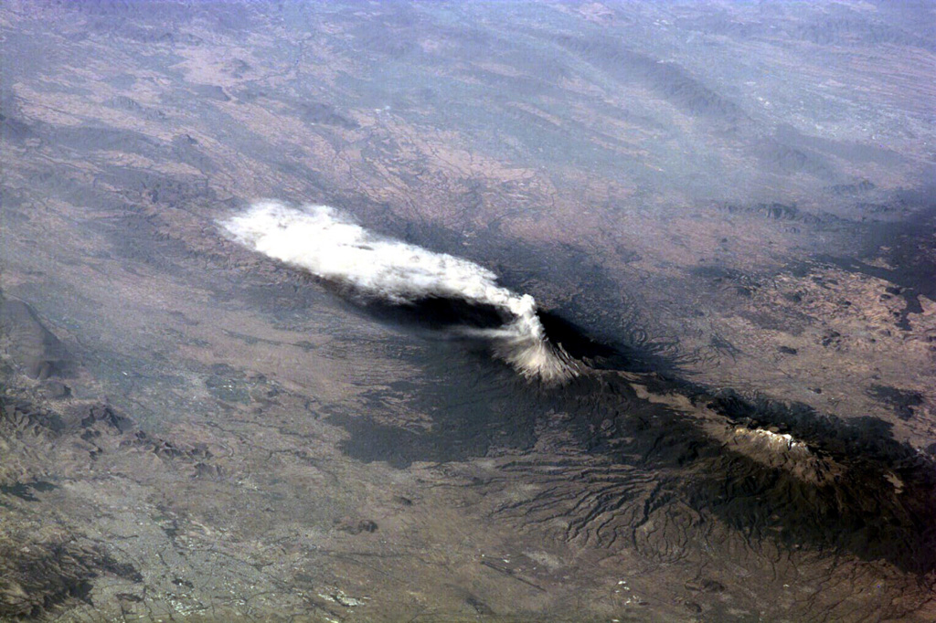 An ash plume from Popocatépetl reaching over 9 km above sea level and dispersing to the south on 23 January 2001. Larger explosions the day before had produced plumes that rose 8 km above the summit and pyroclastic flows that traveled 4-6 km down the north flank. The large dark-colored area below and to the left of the volcano is a lava field. The elongate Iztaccíhuatl volcano is visible to the lower right. Image courtesy of Earth Sciences and Image Analysis Laboratory, NASA Johnson Space Center, 2002 (http://eol.jsc.nasa.gov).