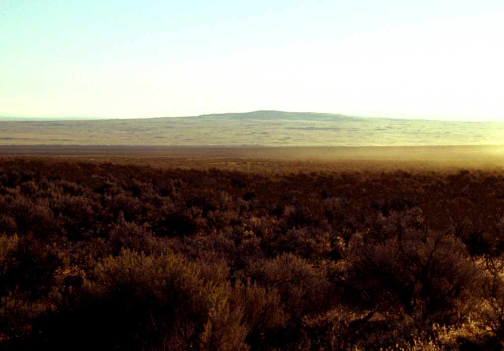 The low shield volcano of Jackies Butte, sometimes referred to as Bowden Crater, is seen here from the SW on the northern side of the Bowden Hills near the SE corner of Oregon.  This small, relatively unstudied basaltic volcanic field consists of two small shield volcanoes and two cinder cones.  The 1418-m-high Jackies Butte lies about 40 and 70 km from the borders with Idaho and Nevada, respectively.  Lava flows of late Quaternary age cover an area of about 325 km2 SE of Burns Junction on Highway 95 and SW of Owyhee Canyon.   Photo by Lee Siebert, 2002 (Smithsonian Institution).