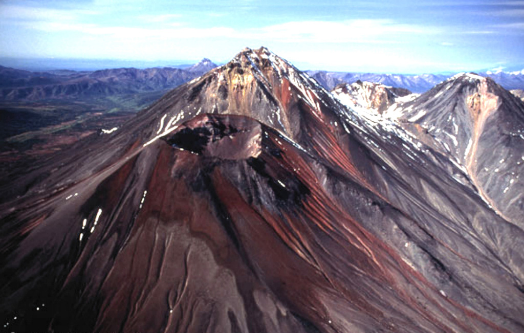 The Gamchen massif, consisting of one Holocene and three late-Pleistocene cones, is seen here from the SE. The reddish Holocene cone in the foreground is Barany and has a 500-m-wide, 200-m-deep crater. Stratigraphic evidence indicates that it grew during several episodes of activity 3,600-3,000 years ago. Yuzhny Gamchen (center) forms the high point of the massif. Kizimen volcano is seen on the distant horizon left of Gamchen's summit. Copyrighted photo by Philippe Bourseiller (Holocene Kamchataka volcanoes; http://www.kscnet.ru/ivs/volcanoes/holocene/main/main.htm).