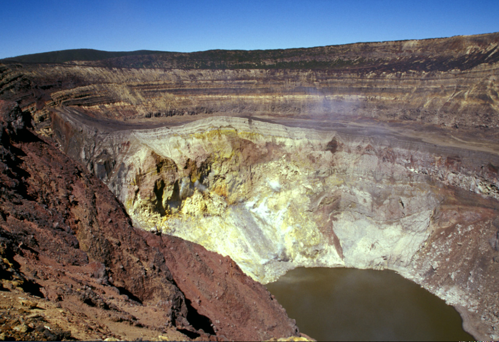Gases rise from the hydrothermally altered western wall of Santa Ana's inner summit crater above the acidic lake. A steep path down the NE crater wall (far right) provides access to the lake for geochemical sampling. Sequences of phreatomagmatic tephra units more than 100 m thick are exposed in the walls of the outer summit craters. Photo by Paul Kimberly, 2002 (Smithsonian Institution).