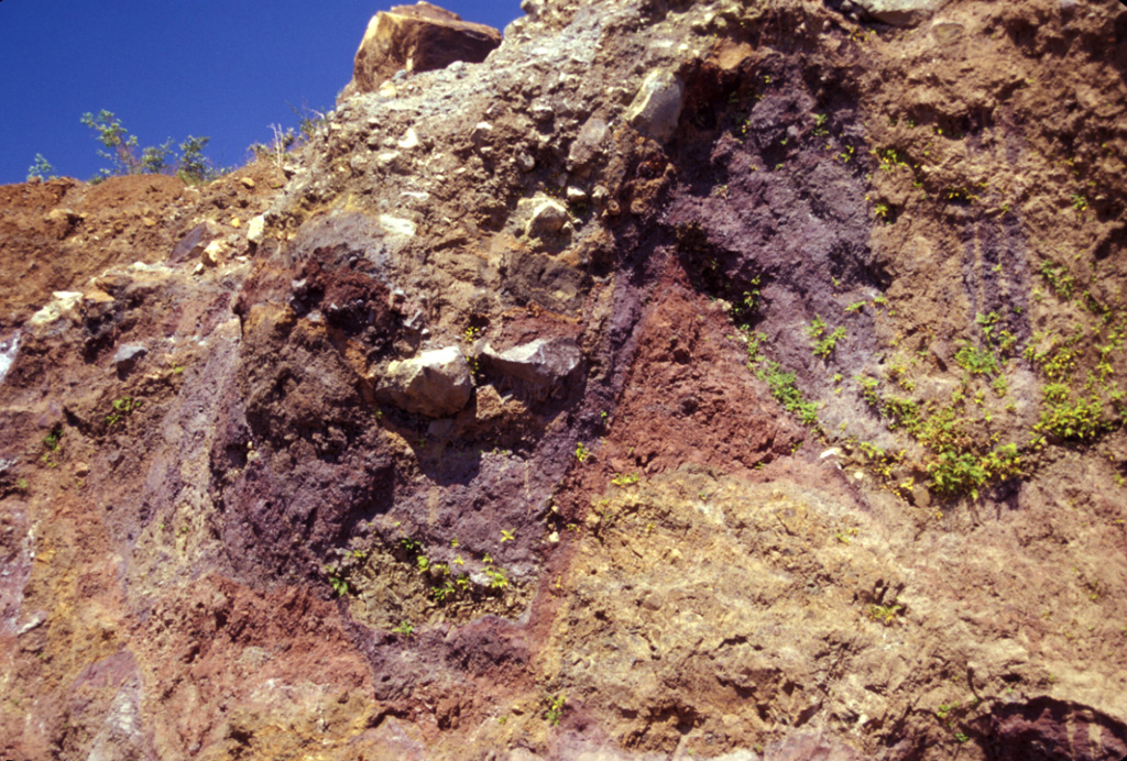 Multi-colored individual units of the Acajutla debris avalanche deposit are offset along normal faults in this view of a quarry wall 6 km SE of the city of Sonsonate. Many blocks are unfractured, and some are shattered blocks with jigsaw textures. About 8 m of the quarry wall is exposed on the right-hand side. The voluminous Acajutla avalanche deposit was produced by late-Pleistocene edifice failure of Santa Ana; this quarry lies about 18 km from the volcano. Photo by Lee Siebert, 2002 (Smithsonian Institution).