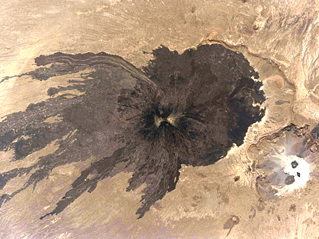 A dramatic Space Shuttle image shows dark lava flows radiating from Toussidé volcano and spreading across the desert floor. Light-colored altered areas can be seen at the summit, the second highest peak of the Tibesti Range in Chad. It was constructed at the W end of the large Pleistocene caldera of Yirrigue, whose E scarp is seen right of Toussidé. The smaller 1-km-deep, 8-km-wide Trou au Natron caldera (lower right) cuts the SE rim of the caldera. NASA Space Shuttle image STS111-367-29, 2002 (http://eol.jsc.nasa.gov/).