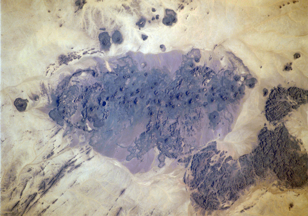 The Bayuda volcanic field is located near the center of the Bayuda desert of NE Sudan. The numerous small scoria cones that trend horizontally across the center of the volcanic field in this International Space Station image were erupted along a WNW-trending line. Lava flows, one of which was erupted about 1,100 years ago, are visible in this image, but about 10% of the vents are craters. Bayuda was constructed over Precambrian and Paleozoic granitic rocks, which form the darker areas at the lower right. NASA International Space Station image ISS004-711-20, 2002 (http://eol.jsc.nasa.gov/).