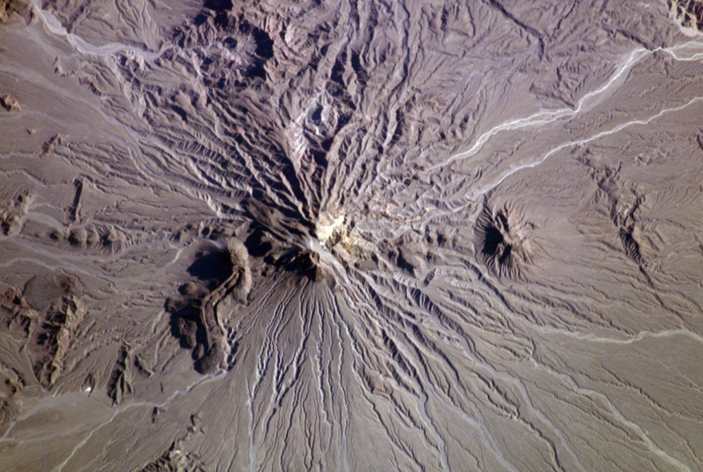 The Bazman (Kuh-e Bazman) volcano is located in remote SE Iran. A well-preserved, 500-m-wide crater caps the summit. Lava domes have been the source of viscous lava flows, including the prominent flow with visible flow levees at the lower left. No historical eruptions are known, but minor fumarolic activity has been reported. NASA International Space Station image ISS006-E-5209, 2002 (http://eol.jsc.nasa.gov/).