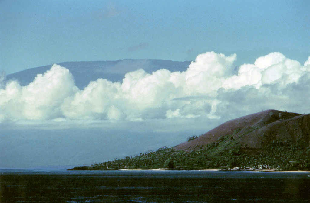 Clouds cover the flanks of the Karthala shield volcano at the S end of Grand Comore Island. A scoria cone of the northern La Grille shield volcano is on the coast in the foreground. Karthala contains a 3 x 4 km summit caldera and elongated rift zones that extend to the NNW and SE from the summit. More than twenty eruptions have been recorded at Karthala since the 19th century, but no historical eruptions are known from La Grille volcano. Copyrighted photo by Stephen and Donna O'Meara, 2002.