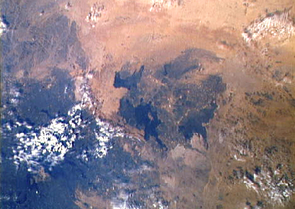 The 4,000 km2 Harrat Ithnayn volcanic field appears in the center of this Space Shuttle image with north to the upper right. Harrat Ithnayn contains scattered shield volcanoes and scoria cones that have produced extensive lava flows, some of which are less than 4,500 years old. Harrat Ithnayn merges with the larger Harrat Khaybar volcanic field to its south, the dark partially cloud-covered area at the lower left. NASA Space Shuttle image STS-61A-483-20 (http://eol.jsc.nasa.gov/).