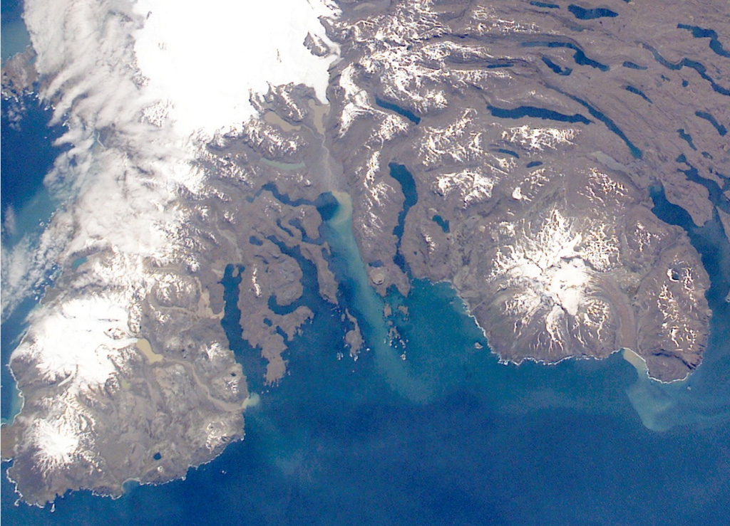 The Rallier du Baty Peninsula (bottom left) forms the SW tip of Kerguelen Island. It contains two subglacial eruptive centers, Mont St. Allouarn and Mont Henri Rallier du Baty. An active fumarole field is related to a series of Holocene trachytic lava flows and lahars that extend beyond the icecap. The snow-covered peak at the mid-right is late-Pleistocene Mount Ross stratovolcano. The Kerguelen Islands are composed primarily of Tertiary flood basalts and a complex of plutonic rocks extensively modified by glaciation. NASA International Space Station image ISS005-E-21805, 2002 (http://eol.jsc.nasa.gov/).