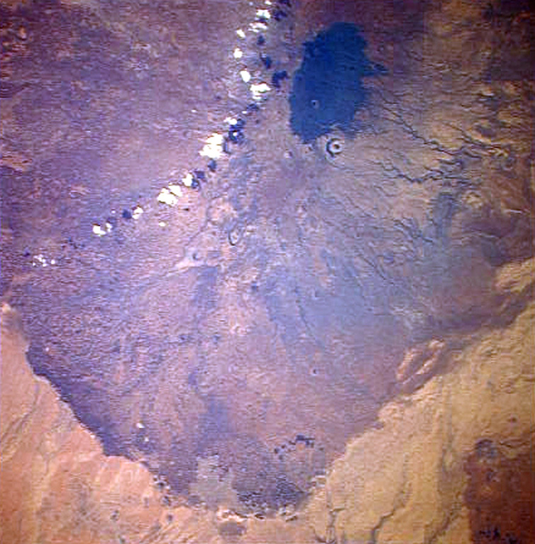 A Space Shuttle perspective shows part of Marsabit, a massive, 6,300 km2 shield volcano located 170 km E of the center of the East African Rift. Its slopes are dotted with 180 cinder cones and 22 maars, such as the prominent circular one below the thickly vegetated summit of the shield volcano. Most of these vents are concentrated along NW- and NE-trending belts cutting across the summit. The youngest lava flows are unvegetated, and the post-shield cinder cones were mapped as Pleistocene to Holocene in age. NASA Space Shuttle image STS026-37-2, 1988 (http://eol.jsc.nasa.gov/).