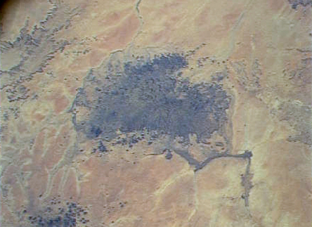 The dark-colored area in the center of this Space Shuttle view is the alkaline Meidob volcanic field in western Sudan. This broad volcanic field covers an area of 5,000 km2 with nearly 700 Pliocene-to-Holocene vents. The margins of the field are dominated by basaltic scoria cones and associated lava flows, but the lava domes, tuff rings, and maars that are concentrated along the central E-W-trending axis of the volcanic field are among the youngest features. The latest dated eruptions took place about 5,000 years ago. NASA Space Shuttle image STS073-713-87, 1995 (http://eol.jsc.nasa.gov/).