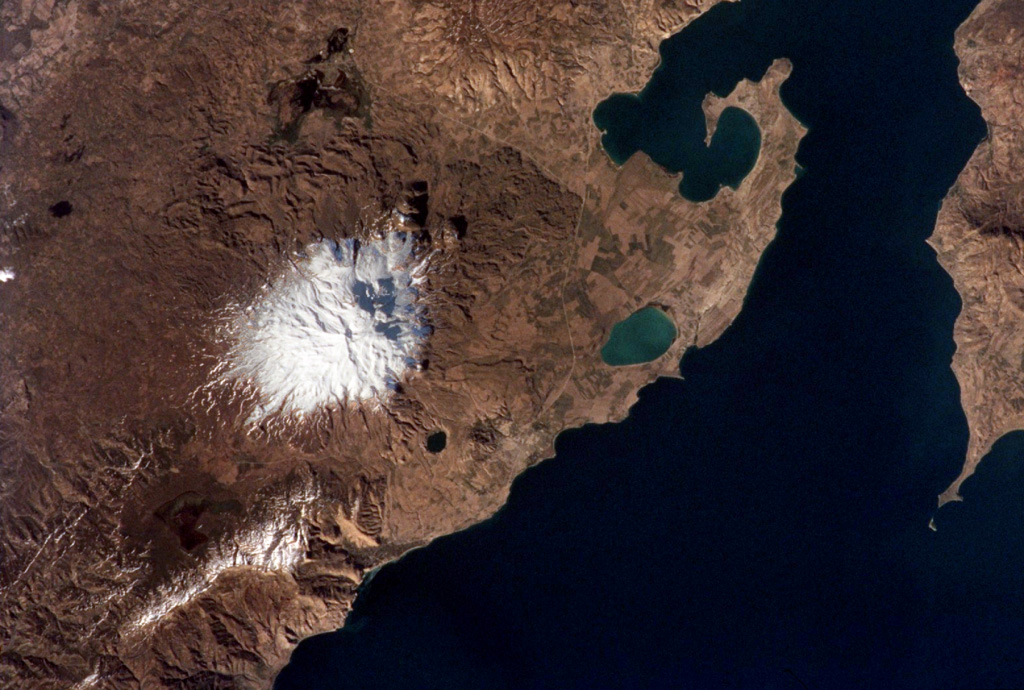 Snow-capped Süphan Dagi volcano seen from the International Space Station, with north to the upper left. The flanks of the volcano contain numerous lava domes and cones that erupted along radial and circumferential fissures. The small black lake halfway between the snow line and Lake Van is the 1.5-km-wide Aygirgölü maar; the larger greenish Lake Arin is visible to the east. NASA International Space Station image ISS002-313-9, 2001 (http://eol.jsc.nasa.gov/).