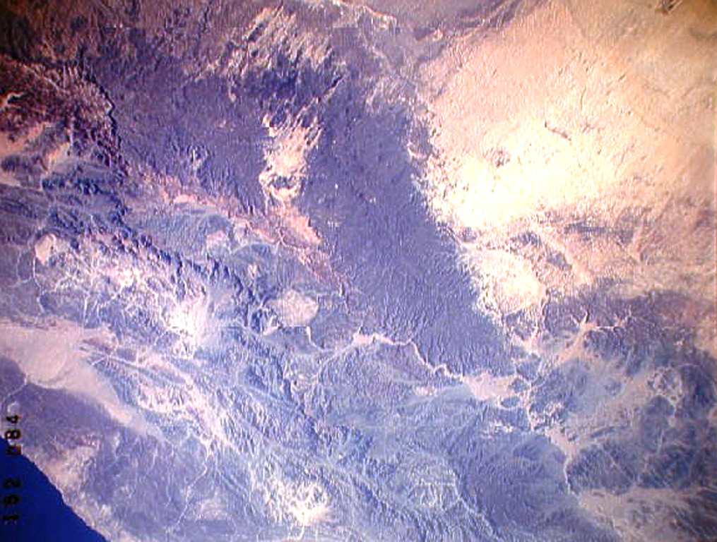 The large dark wedge-shaped area near the center of this Space Shuttle image is Harrat 'Uwayrid, a major volcanic field in NW Saudi Arabia that contains basaltic scoria and tuff cones. Bedouin legends say that Hala-'l-Bedr erupted fire and stones in 640 CE, killing herdsmen and their cattle and sheep. Another volcanic field, Harrat ar Rahah (top-left), lies to the NW. NASA Space Shuttle image STS37-152-84, 1991 (http://eol.jsc.nasa.gov/).