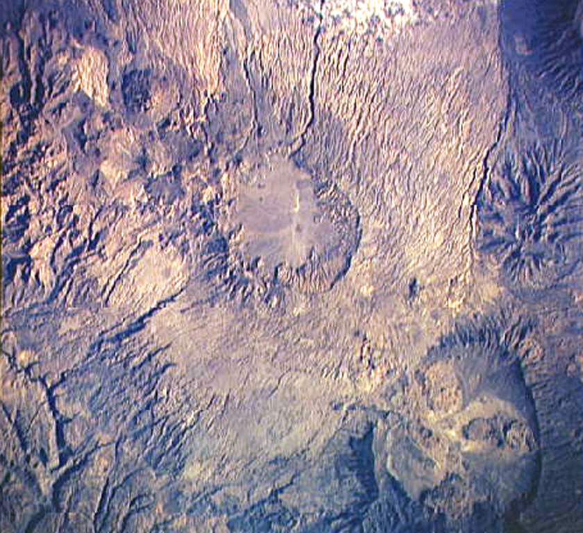 The circular area near the center of this Space Shuttle image is the shallow 14 x 18 km wide summit caldera of Tarso Voon volcano in the west-central part of the Tibesti Range. Quaternary basalts were erupted from vents near the caldera rim and from Ehi Mousgau, a small stratovolcano visible to the NW. The large Soborom solfatara field west of the massif, with its active mud pots and boiling waters, is visited by Tibesti peoples for medicinal uses. Pleistocene Tarso Yéga caldera to the SE is at the lower right. NASA Space Shuttle image STS41B-42-2521 1984 (http://eol.jsc.nasa.gov/).