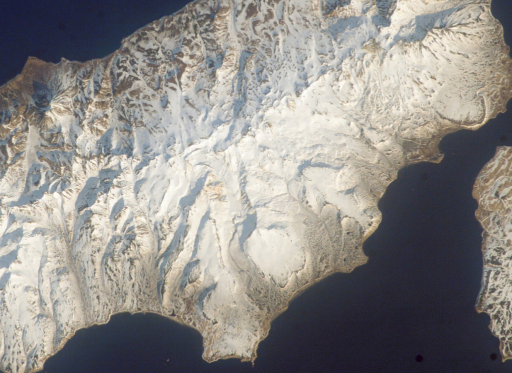 The Vernadskii Ridge descends diagonally across this Space Shuttle image of northern Paramushir Island (with N to the upper right). The ridge is comprised of the Vernadskii (south) and Bogdanovich (north) volcano groups, consisting of small cones and lava domes. The historically active Ebeko volcano lies at the far upper right. The three large smooth-textured surfaces along the Pacific coast (to the right) are pre-glacial Pleistocene lava flows. NASA International Space Station image ISS004-E-611695, 2002 (http://eol.jsc.nasa.gov/).