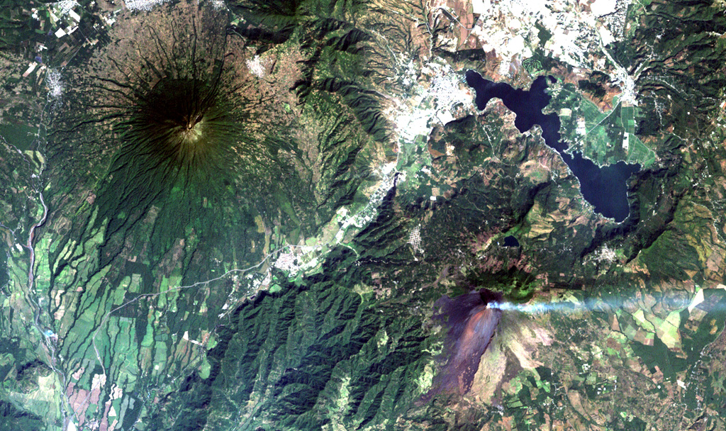 Steaming Pacaya volcano (lower right) lies across a valley from symmetrical Agua volcano (upper left).  Pacaya was constructed near the southern margin of Amatitlán caldera, whose SE rim lies near the right-center margin.  The 14 x 16 km wide caldera was formed during a series of major silicic explosive eruptions between about 300,000 and 23,000 years ago.  The irregular margins of Lake Amatitlán are constrained on the SW side by post-caldera lava domes.  The outskirts of Guatemala City lie at the upper right. NASA Landsat image, 2000 (courtesy of Loren Siebert, University of Akron).
