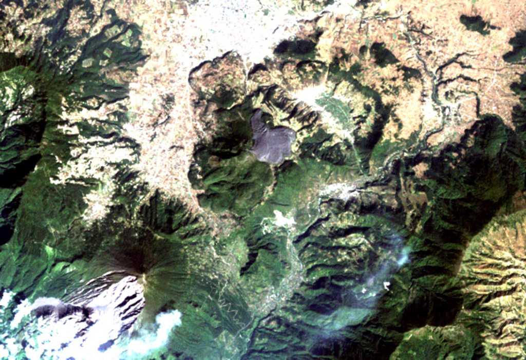 The arcuate area at the top center below the light-colored city of Quetzaltenango is the Almolonga volcanic complex.  An arcuate series of lava domes outlines the northern part of the complex, while the unvegetated area to the south is the 1818 lava flow from Cerro Quemado volcano, the youngest of the Almolonga complex.  Almolonga is located along the Zunil fault zone, which extends diagonally SW along the Río Samalá (bottom-center).  The furrowed 1902 crater of Santa María volcano lies at the lower left. NASA Landsat image, 2000 (courtesy of Loren Siebert, University of Akron).