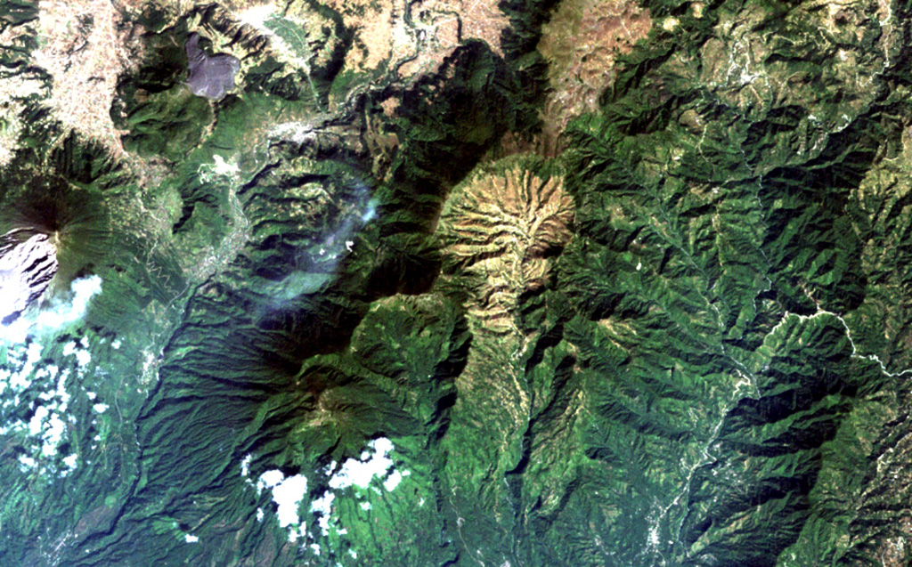 The light-colored, furrowed area at the top-center is the 4-km-wide, 600-m-deep Tzanjuyub caldera, which is breached to the south by the Río Masa.  At the SW side of the Pleistocene caldera is Volcán Zunil, which is connected by an irregular ridge to Volcán Santo Tomás, a large eroded stratovolcano above the clouds at the bottom of the image.  Santa María volcano (far left-center) lies across the Río Samalá to the east.  Solfataras and thermal springs are located on the west side of the ridge between Santo Tomás and Zunil. NASA Landsat image, 2000 (courtesy of Loren Siebert, University of Akron).