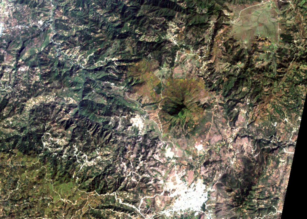 The smooth-textured area displaying a radial drainage pattern at the right-center is Jumay volcano in SE Guatemala.  The volcano was constructed near the contact between Tertiary volcanic rocks on the south and Paleozoic metamorphic rocks on the north.  The 2176-m-high volcano lies immediately north of the large city of Jalapa (the light-colored area at the bottom right). NASA Landsat image, 2000 (courtesy of Loren Siebert, University of Akron).