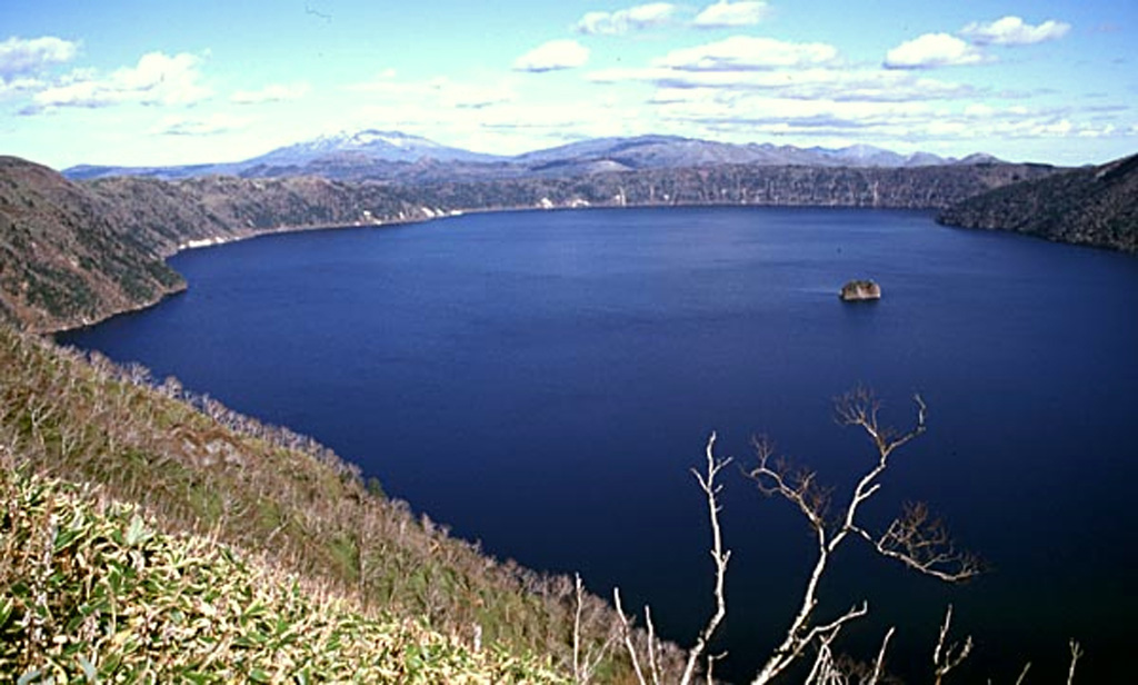 The deep blue waters of 6-km-wide Mashu caldera are seen here from its western rim. The small island of Kamuishu in the center of Lake Mashu (right-center) is the tip of a mostly submerged lava dome. Mashu is a Holocene caldera of a volcano constructed on the ESE rim of the Kussharo caldera. Following caldera collapse, Kamuinupuri (whose lower flanks are visible at the far right) formed beginning about 4,000 years ago.  Copyrighted photo by Shun Nakano, 2001 (Japanese Quaternary Volcanoes database, RIODB, http://riodb02.ibase.aist.go.jp/strata/VOL_JP/EN/index.htm and Geol Surv Japan, AIST, http://www.gsj.jp/).