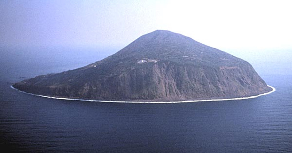 Steep cliffs up to 300-m-high surround the small island of Toshima. Toshimamura, the port village of the island, is to the far left in this view from the west. Toshima lies about 20 km W of the main volcanic front of the Izu-Marianas arc. Recent activity occurred between about 8,000 and 40,00 years ago. Copyrighted photo by Shun Nakano (Japanese Quaternary Volcanoes database, RIODB, http://riodb02.ibase.aist.go.jp/strata/VOL_JP/EN/index.htm and Geol Surv Japan, AIST, http://www.gsj.jp/).