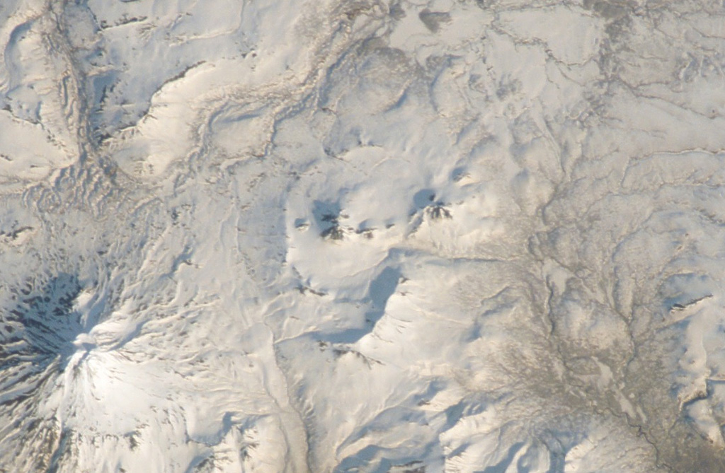 The circular caldera at the center of this International Space Station image with N to the upper right is Pizrak caldera. The Holocene Kell volcano is visible within the caldera. This remote volcanic complex in southern Kamchatka contains three partially nested 3-5 km wide calderas containing lava domes and cones, of which Kell is the highest. The larger edifice to the lower left is Zheltovsky. NASA International Space Station image ISS004-E-11700, 2002 (http://eol.jsc.nasa.gov/).
