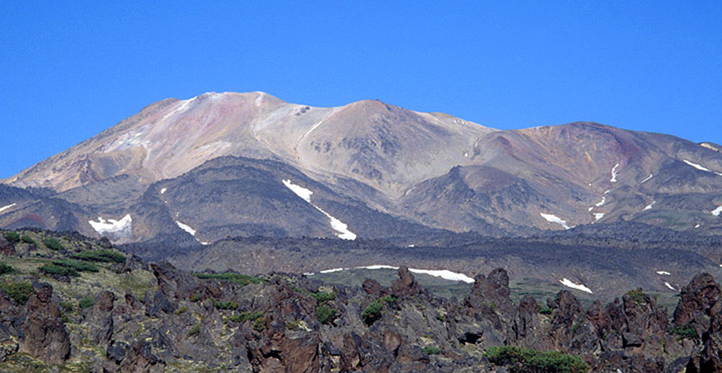 Hydrothermally altered rocks form the summit ridge of Komarov in this view from the east. Komarov is a complex structure in the northern half of the Gamchen ridge and lies at the western end of a 2.5 x 4 km caldera. Holocene lava flows, such as the one in the foreground, extend beyond the caldera to the east and west.  Copyrighted photo by Vera Ponomareva (Holocene Kamchataka volcanoes; http://www.kscnet.ru/ivs/volcanoes/holocene/main/main.htm).