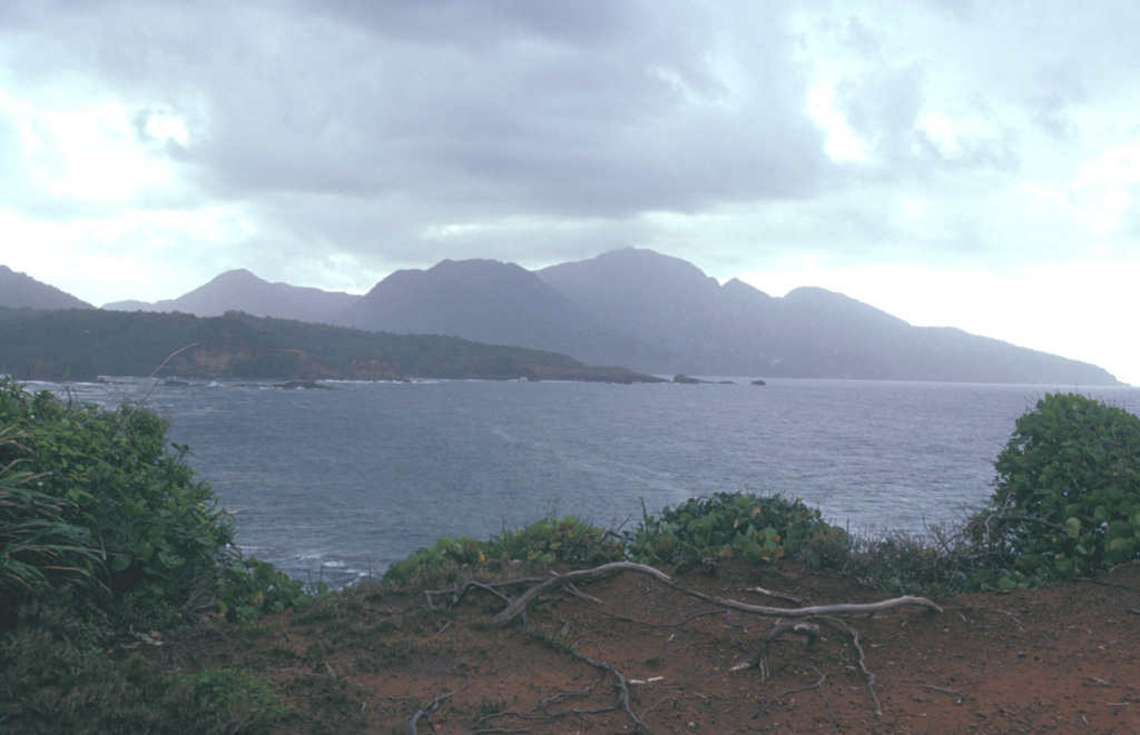Morne aux Diables volcano rises above the Atlantic coast of NW Dominica.  The summit of the volcano is formed by a complex of lava domes, and flank domes, which extend in a roughly E-W chain across the southern flank of the volcano, are visible on the left horizon.   Photo by Paul Kimberly, 2002 (Smithsonian Institution).