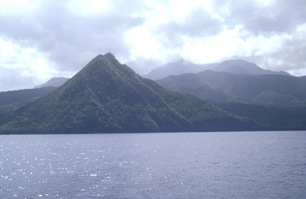 Morne Espagnol, also known as Barbers Block, is a steep-sided Pliocene lava dome that rises to 365 m above the coast on the NW flank of Morne Diablotins volcano, whose summit is hidden in the clouds.  The massive volcano, the largest on Dominica, is capped by a complex of at least five lava domes.  Block-and-ash flow deposits radiate away from the summit and reach the coast.  Photo by Lee Siebert, 2002 (Smithsonian Institution).