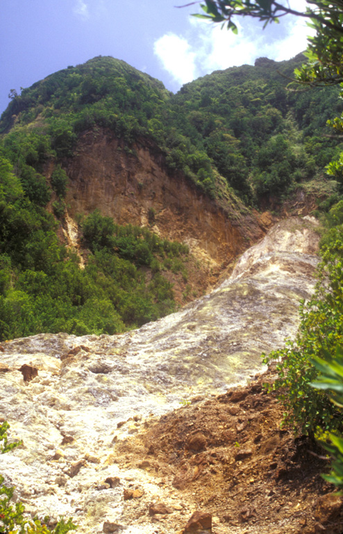 The upper Sulphur Springs geothermal area cuts the SW flank of Morne Plat Pays stratovolcano and lies just inside the large scarp formed by collapse of the edifice.  The thermal area consists of steaming, hydrothermally altered ground with yellowish area marking many sulfur-encrusted fumaroles with temperatures of from 90-100 degrees Centigrade measured during the past century.  Minor hot springs are also present.   Photo by Lee Siebert, 2002 (Smithsonian Institution).