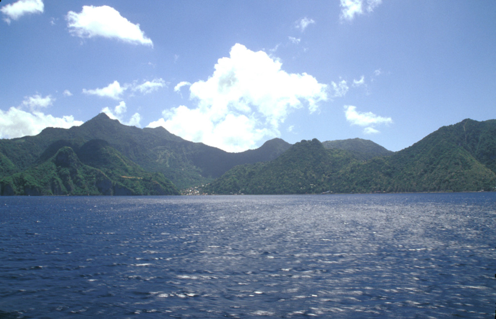 Morne Plat Pays (left), Morne Patates (right-center) and Crabier (right) at the SW tip of Dominica are seen from the SW.  The Morne Plat Pays volcanic complex contains the Morne Plat Pays stratovolcano and a complex of central lava domes.  The complex is cut by a large depression, partly filled by the lava domes, that was formed by collapse of the volcano during the late Pleistocene.  The collapse scarp is 400-900 m high, and submarine debris-avalanche blocks from the collapse are visible in bathymetry. Photo by Paul Kimberly, 2002 (Smithsonian Institution).